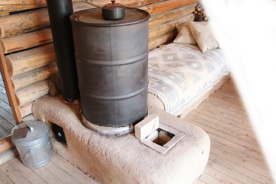 A cob rocket mass heater and cushioned thermal-mass bench inside a log cabin